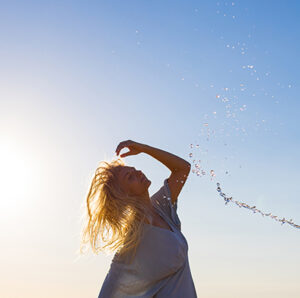 femme blonde en robe bleu devant un ciel bleu dont la silhouette est soulignee par un filet d'eau.