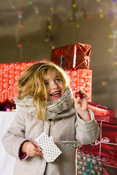 petite fille blonde qui trouve une boule de noel dans une boite entoure de cadeaux.