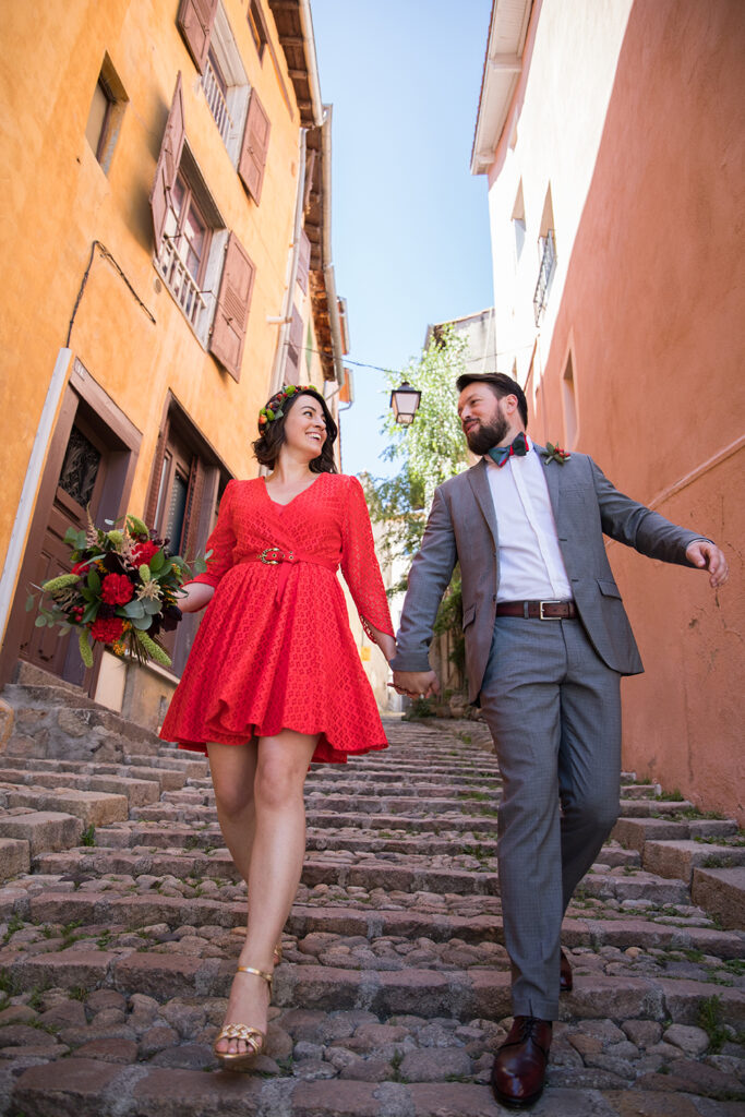 reportage mariage dans la loire : une mariee en robe rouge et son epoux en costume gris descendent les marches des escaliers paves des petites rues de la ville.